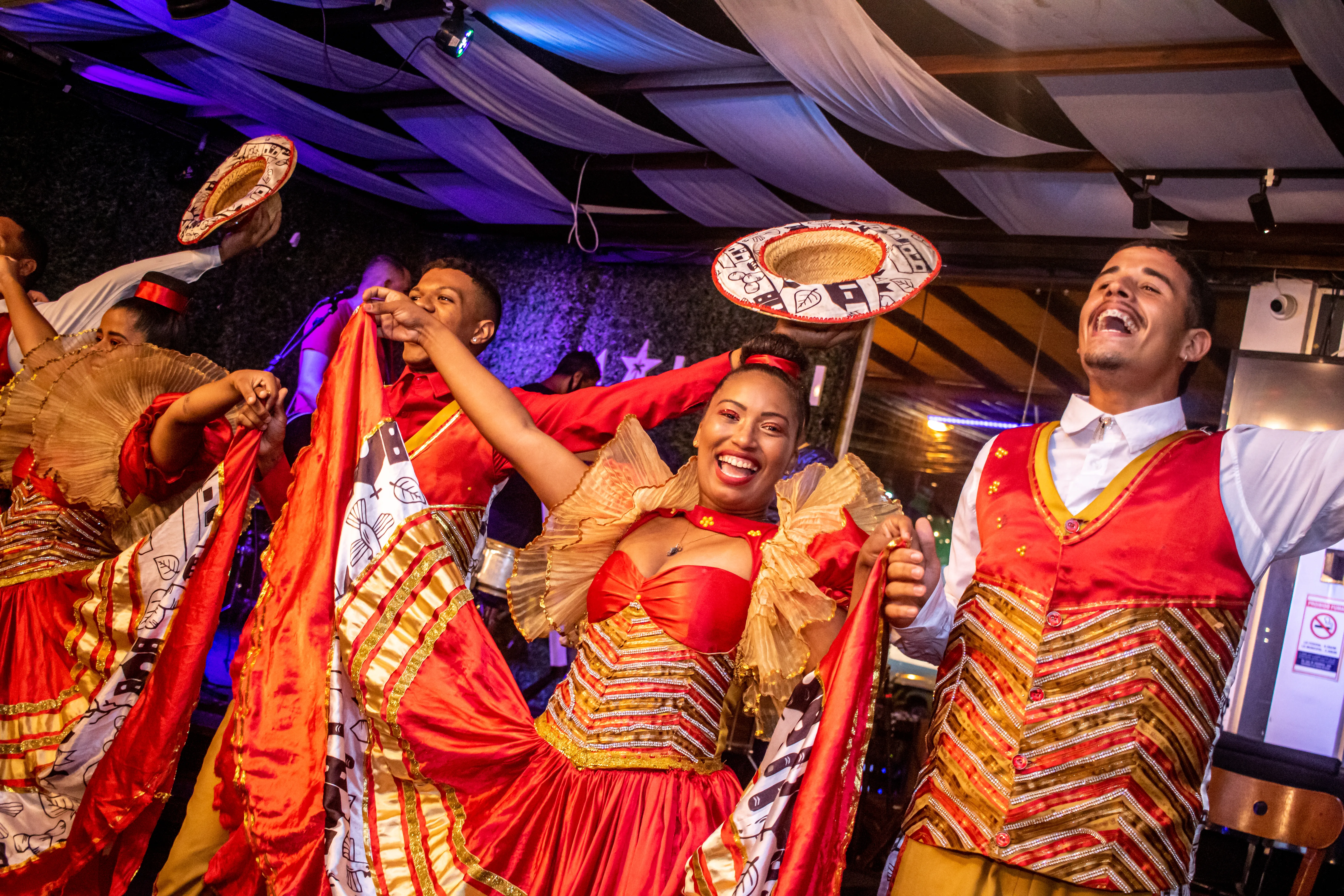 Dançarinos em trajes vermelhos e dourados na Noite do Turista no Maikai Show Bar